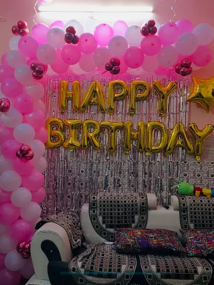 A pink and white themed birthday decoration with a balloon arch over a silver shimmer curtain.