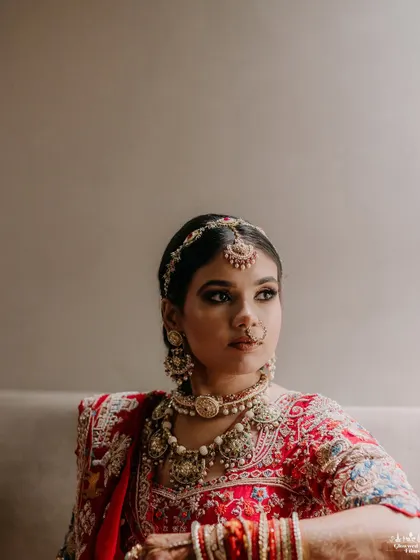 A classic, elegant portrait of the bride, Sakshi, looking away thoughtfully, her intricate jewelry and red lehenga beautifully captured.