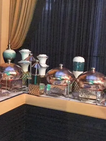 A corner view of a buffet line featuring a mix of copper and silver chafing dishes, accented with elegant turquoise and white vases for a pop of color.