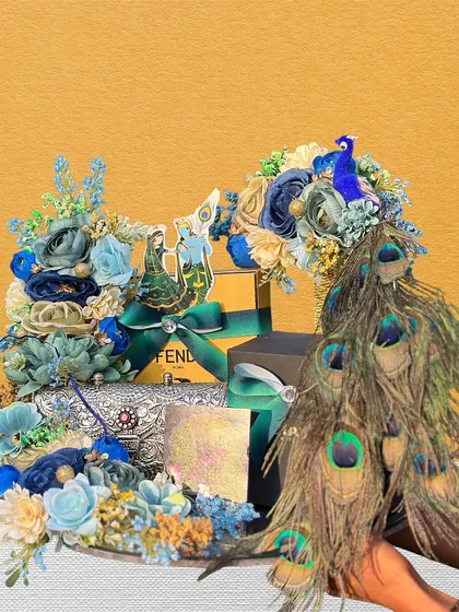 A stunning Teej hamper featuring a silver box and a Fendi package. The arrangement is decorated with a large peacock feather spray and a beautiful blue and cream floral design.