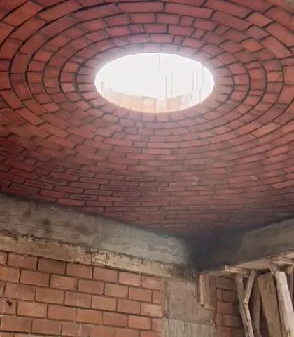 A completed brick dome with a central skylight, seen from the inside during construction. The pattern is both structural and beautiful.