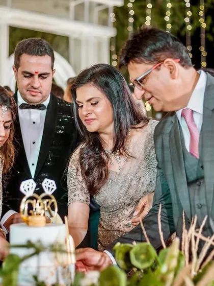 The couple and their parents at the cake-cutting ceremony. A classic family portrait marking a happy milestone.