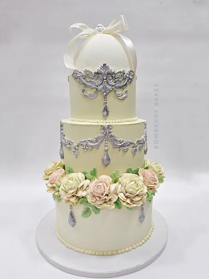 This vintage-style engagement cake features a unique, fully edible ring holder on top, perfect for a surprise proposal. The design combines delicate buttercream piping with beautiful pastel flowers for a timeless look.