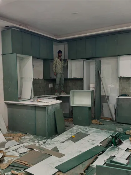 The kitchen during the cabinet installation phase. You can see the green laminate carcasses being fitted before the shutters are installed.