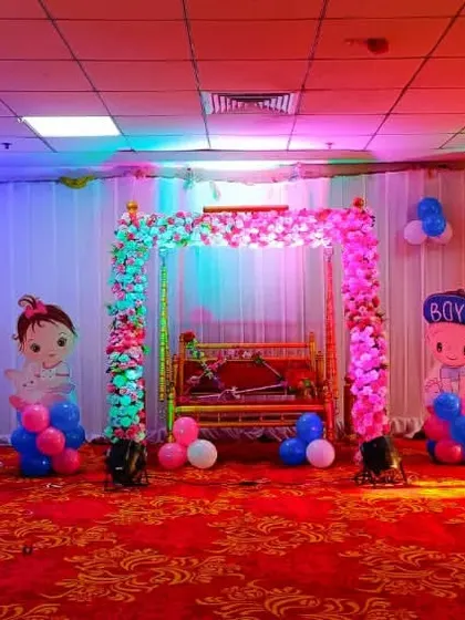 For a larger hall, I created this complete stage decoration for a naming ceremony. It includes a decorated cradle, a large floral moon prop for photos, baby character cutouts, and pink and blue balloons for a classic baby theme.
