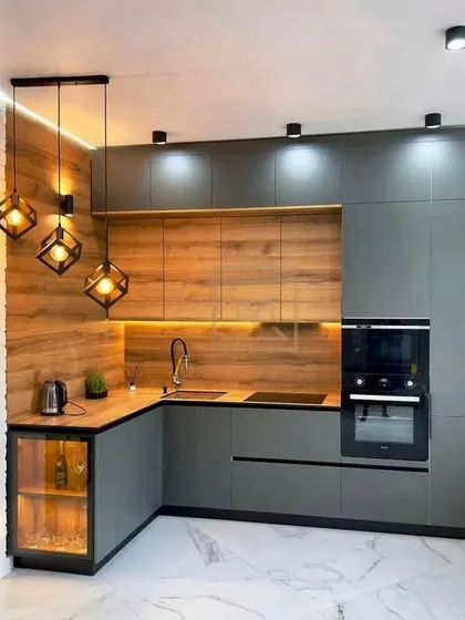 A modern L-shaped kitchen featuring a mix of grey and wood-textured cabinets. The geometric pendant lights and a small glass-front corner cabinet add unique design elements.