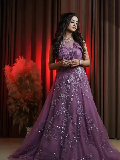 This shot captures the full silhouette of the onion pink gown against a rich, dark curtain, highlighting the sparkle of the embroidery. A perfect rental for an evening event.