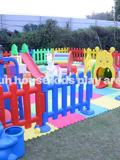A full outdoor setup of the rainbow play area, fenced in for safety, with a ball pit, slide, tunnel, and rockers.