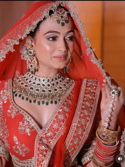 A close-up of a bride in a classic red lehenga, focusing on the stunning emerald and kundan jewellery set that completes the look.