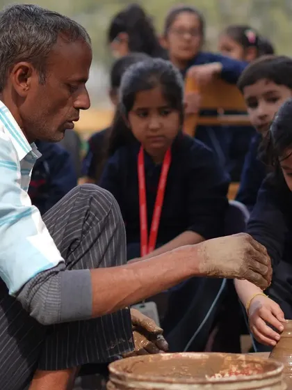 A pottery instructor guiding a young student at the potter's wheel during a school trip.