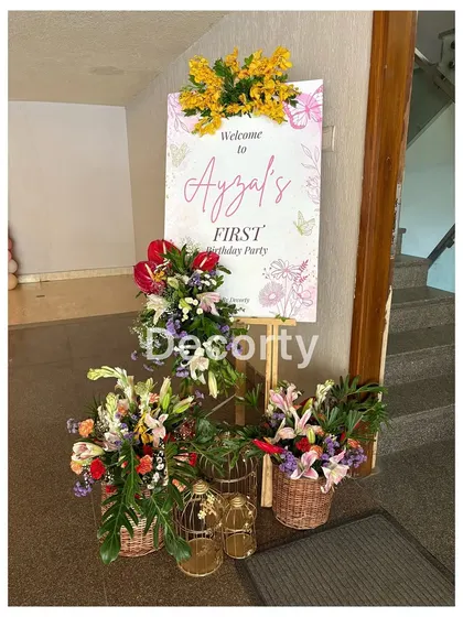 An elegant welcome sign for 'Ayzal's First Birthday Party', surrounded by beautiful fresh flower arrangements.