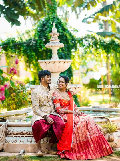 A classic romantic portrait of a couple in traditional outfits by a garden fountain.