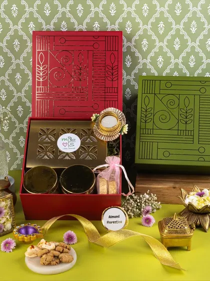 A colorful composition of red and green festive boxes, styled with fresh flowers and brass elements to highlight the brand's unique packaging.