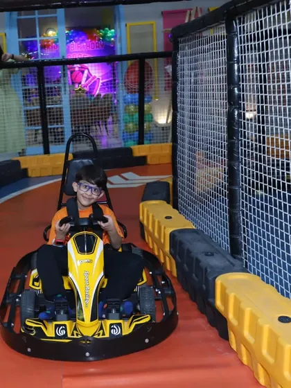 This young racer is enjoying the view from his go-kart, with the track and safety nets visible in the background.