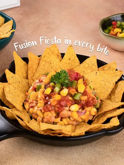 Our unique Nachos Chaat is a fun fusion dish. Crispy tortilla chips are topped with a fresh salsa of corn, onions, and tomatoes, creating a fiesta in every bite.