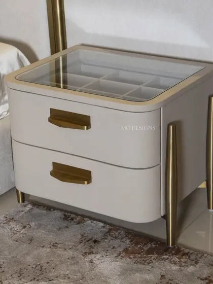 The Solitaire bedside table is a testament to both design and functionality. It features a beautiful glass top revealing a partitioned storage compartment, sleek metal legs, and drawer pulls that match the bed's metal accents.