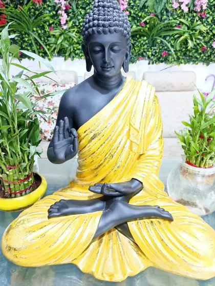 This unique Buddha statue features a black body with a contrasting yellow robe. It's a modern take on a classic symbol of peace.