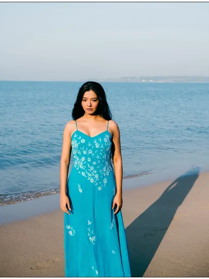 A simple and beautiful full-length portrait against the vastness of the ocean. The composition is clean and focuses on the model.
