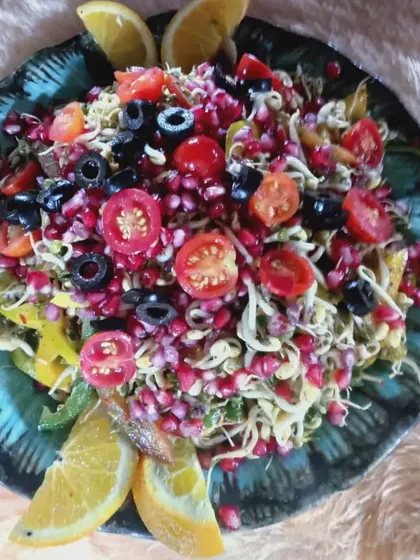 A colorful sprout salad loaded with fresh pomegranate, cherry tomatoes, and black olives, served in a unique turquoise ceramic dish.