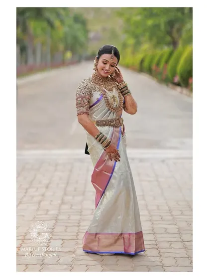 A full-length shot of Vishnu Priya. The off-white and purple saree is a classic choice, and her entire look is styled to perfection, including the traditional saree drape.