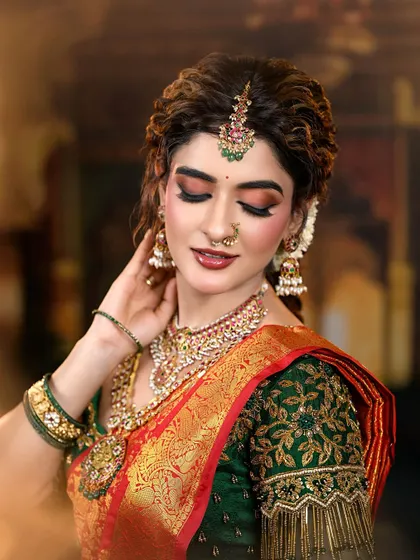 A regal and traditional bridal look featuring a rich red and green Kanjivaram saree. The makeup is defined by warm, shimmery eyes and a deep red lip, perfectly accessorized with temple jewelry.