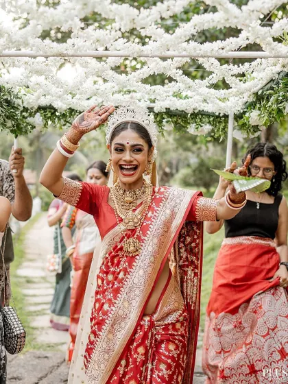 A joyful Bengali bride makes her entrance under a 'phoolon ki chadar' made of white flowers.