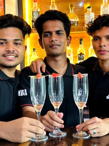 Three students proudly hold up their garnished glasses, ready for the next step in their cocktail-making class.