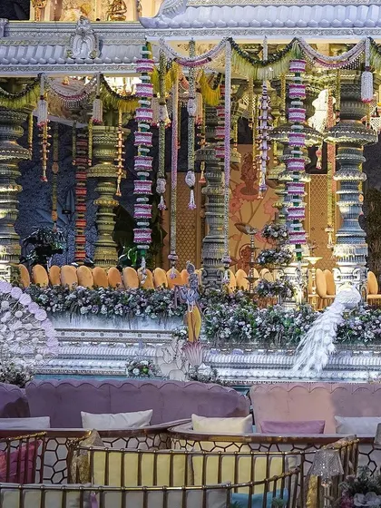 An opulent mandap designed for 'The Eternal Krishna' theme. The stage is flanked by majestic pillars and features statues of peacocks, all set against a backdrop of intricate traditional artwork.