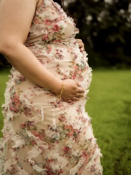 A close-up on the texture of the floral dress against the baby bump, a beautiful detail shot that celebrates both fashion and pregnancy.