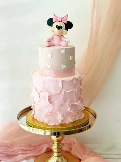 A lovely two-tiered cake with a baby Minnie Mouse topper. I used a soft pink ruffle effect on the bottom tier and a simple heart pattern on top for a gentle, sweet design.