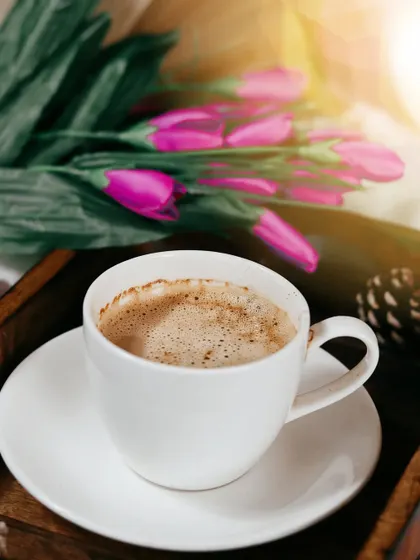 A tight shot of the coffee cup, with pink tulips softly blurred in the background. This composition uses color and depth to create a beautiful and romantic mood.