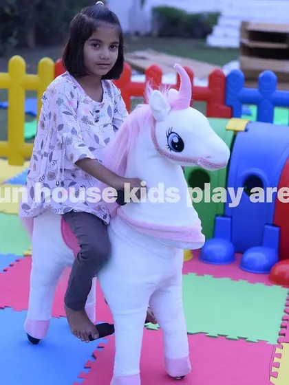 A girl enjoying a ride on the plush unicorn toy within the play area.