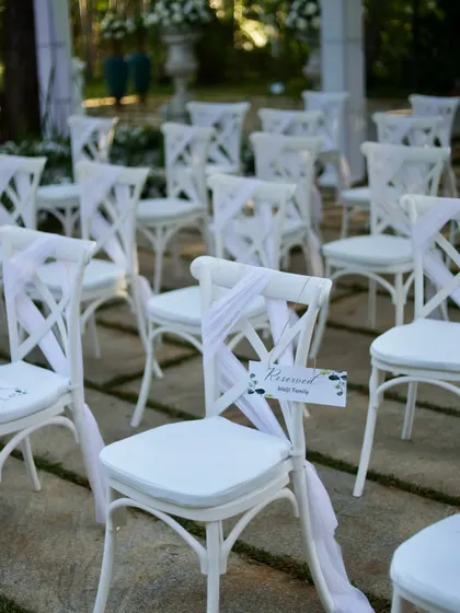 Elegant white cross-back chairs reserved for family, adorned with simple white drapes for a clean and sophisticated look.