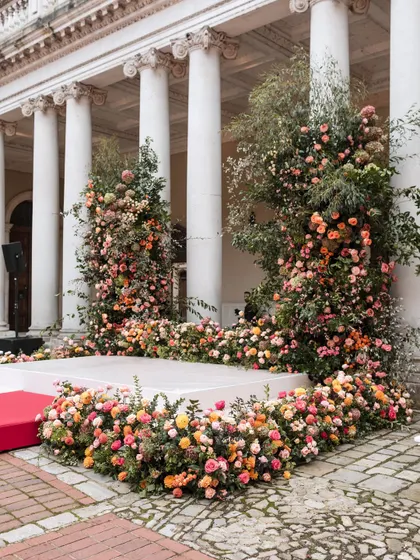 A lush, organic floral mandap set against the classical columns of a historic English palace. We love the contrast of vibrant, wild-feeling flowers with formal architecture.