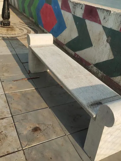 A simple and elegant backless stone bench with scrolled ends, placed on a paved public walkway.