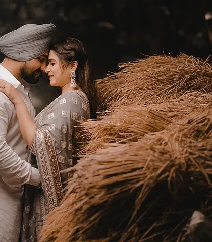 An intimate portrait of Aman and Simran next to a stack of hay. The rustic setting and their close embrace create a warm, earthy, and romantic image that feels straight out of a Punjabi love story.