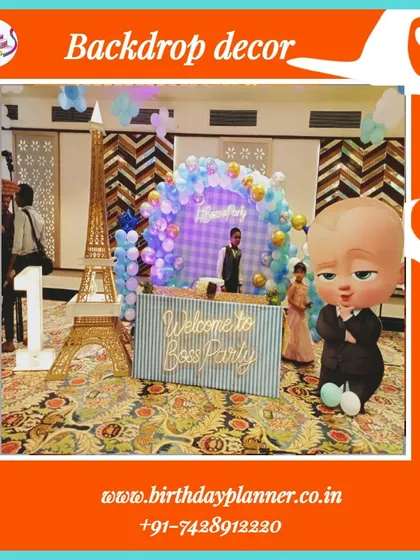 A full view of a Boss Baby party setup, showing the backdrop, character props, and marquee numbers on a patterned carpet, giving a sense of the event space.