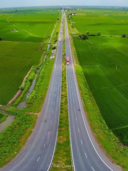 An impressive aerial drone shot of a highway cutting through vibrant green fields, showcasing a symmetrical and powerful perspective.