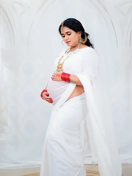 A side profile showcasing the baby bump. The makeup is kept minimal and elegant to fit the pure and serene concept of this beautiful white-themed maternity shoot.