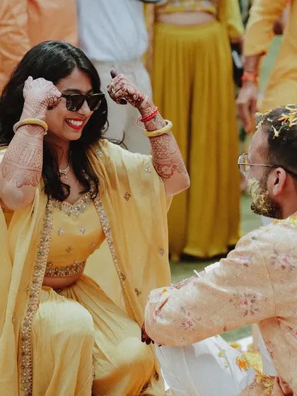 The bride, wearing cool sunglasses, shares a laugh with the groom during their Haldi ceremony.