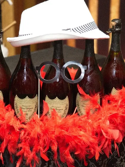 A fun and quirky display of champagne bottles dressed up with a fedora and feather boa. It's a playful touch for a milestone birthday or New Year's Eve party.