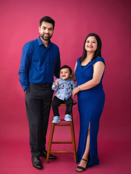 A vibrant and joyful family portrait. The family's royal blue outfits stand out beautifully against the solid magenta background, creating a bold and memorable image.