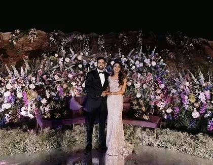 The couple stands on the reception stage, surrounded by an abundance of exotic flowers set against the custom-made mountain backdrop. This showcases the scale and romanticism of our designs.
