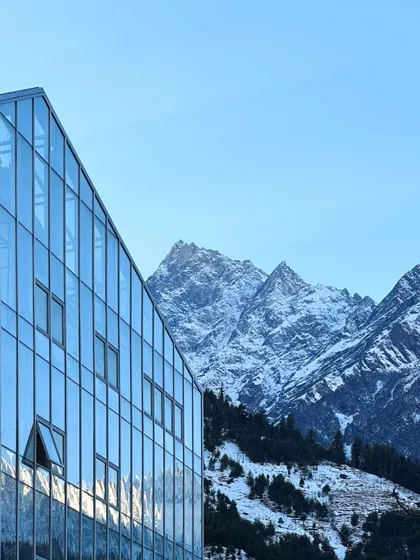 The Hamsa Resort in Manali features a modern glass and steel facade that reflects the surrounding Himalayan peaks. This design choice creates a direct visual dialogue between the structure and its environment, while the building itself incorporates traditional Kathkuni construction principles.