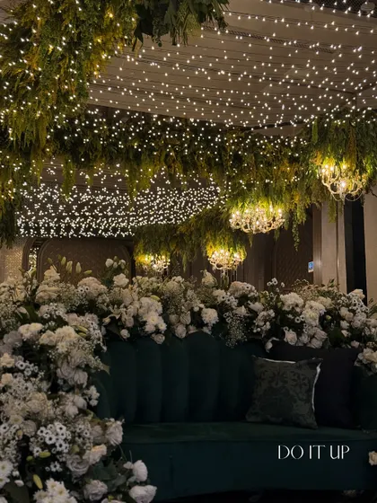 A closer look at the sangeet seating, where a green velvet sofa sits under a canopy of hanging ferns and thousands of fairy lights, creating the feeling of a magical, enchanted forest.