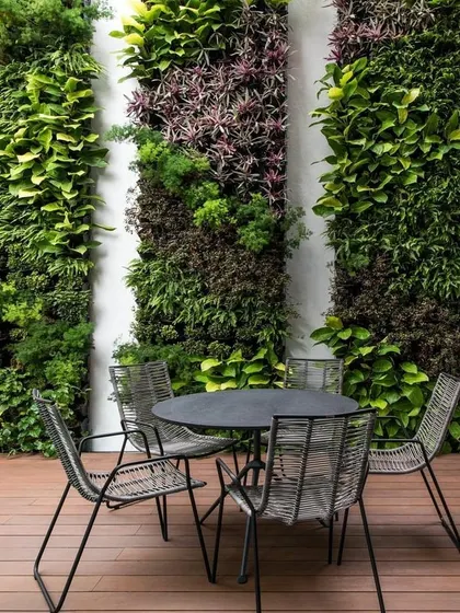 A stylish patio setup with modern outdoor furniture placed in front of several vertical garden panels, creating an intimate and green dining space.