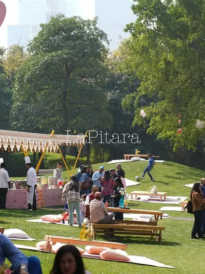 A wide shot of the lively picnic, showing multiple food tents and guests relaxing on the lawn.