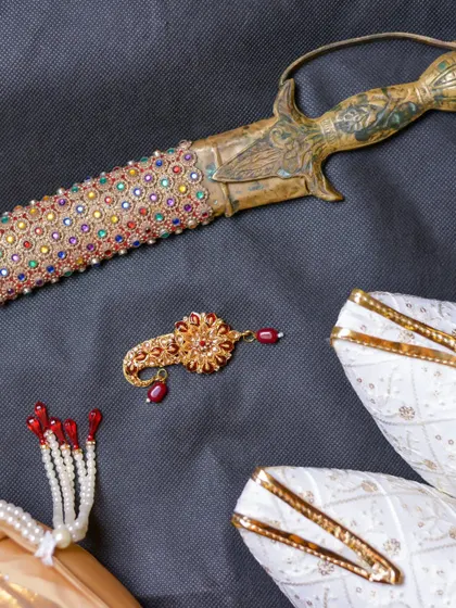 A flat-lay of the groom's royal accessories, including his embroidered shoes (mojari), turban pin (sarpech), and ceremonial sword.