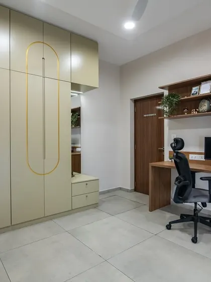 A spacious home office with a long wooden desk and an ergonomic chair. The room includes floor-to-ceiling wardrobes with unique gold inlay details, providing extensive storage while maintaining a clean, sophisticated look.