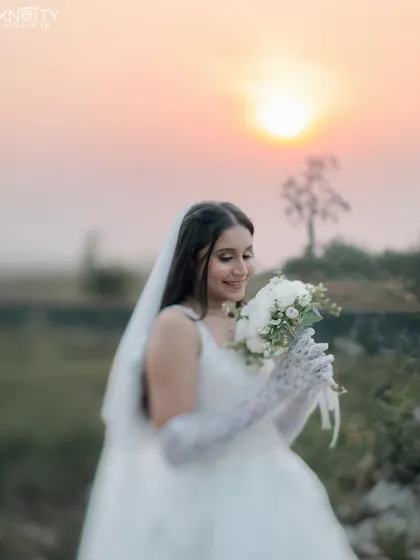 A beautiful bridal portrait at sunset, with the bride holding her bouquet. The golden hour light creates a soft, dreamy, and romantic mood.